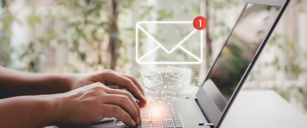 Eine Person sitzt am Laptop und ein Mail Symbol leuchtet aus der Tastatur raus