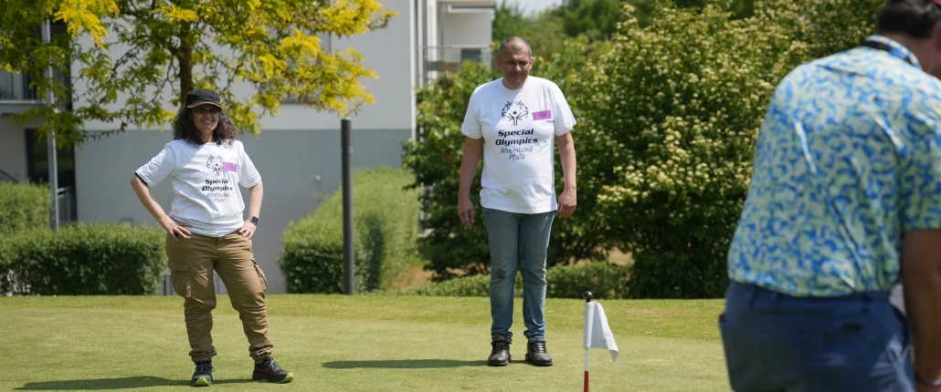 Eine Person spielt Golf und zwei andere schauen zu